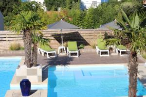 une piscine avec des chaises et des palmiers dans une cour dans l'établissement Hôtel Mer et Forêt, à Saint-Trojan-les-Bains