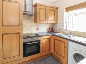 a kitchen with wooden cabinets and a sink and a dishwasher at 2 Organsdale Cottages in Kelsall Hill