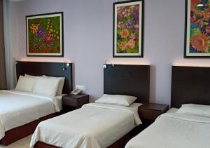 three beds in a room with paintings on the wall at Hotel Desaru Penawar in Desaru