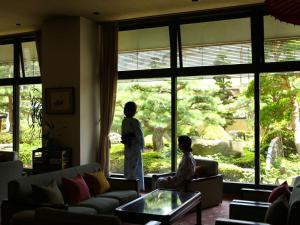 dos personas de pie en una sala de estar mirando por la ventana en Kamiyamada Hotel, en Chikuma