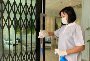 una mujer con una máscara facial y guantes blancos abriendo una puerta en K Maison Boutique Hotel, en Bangkok