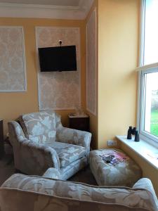een woonkamer met een bank, een stoel en een flatscreen-tv bij Min y Don Guest House in Llanfairfechan