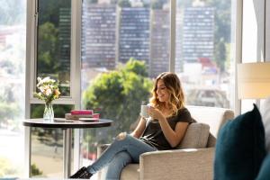 a woman sitting on a couch holding a cup of coffee at Hotel bh Bicentenario in Bogotá