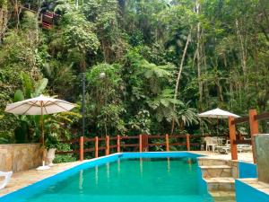 a pool in the middle of a garden with an umbrella at Espaço Viverde Penedo in Penedo
