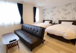a hotel room with two beds and a leather couch at Cozy Inn OTARU in Otaru