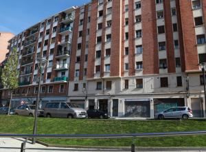 a large brick building with cars parked in front of it at Cálido Apartamento Céntrico Junto Funicular y Metro BY Urban Hosts in Bilbao