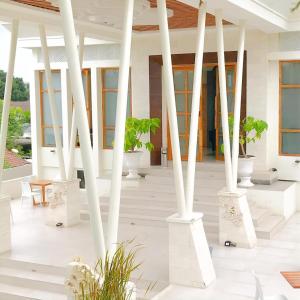 a white porch with white columns and potted plants at Luminor Hotel Banyuwangi By WH in Banyuwangi