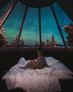 a woman sitting on a bed in front of a window at Wilderness Hotel Inari & Igloos in Inari