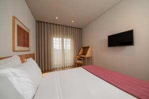 a bedroom with a large white bed with a flat screen tv at Montebelo Principe Perfeito Viseu Garden Hotel in Viseu