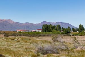 a field with a building and mountains in the background at Hostería El Galpón Del Glaciar in El Calafate