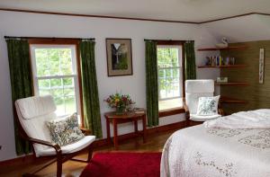 Schlafzimmer mit 2 Stühlen, einem Bett und Fenstern in der Unterkunft Enfield Manor Bed&Breakfast and Vacation Rental in Newfield