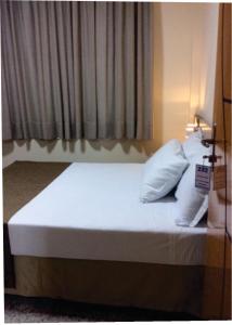 a bed with white sheets and pillows in a room at Hotel Itabira in Itabira