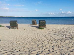 3 sillas sentadas en una playa de arena cerca del agua en Ferienwohnung Cora, en Glücksburg