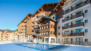 an apartment building with a swimming pool in the snow at Vacancéole - Résidence La Turra in Valfréjus
