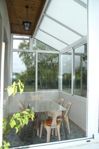 uma mesa de vidro e cadeiras num alpendre com janelas em Gîte les Hortensias em Boulleret