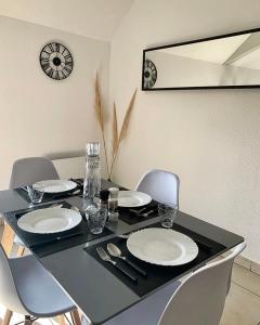 una mesa negra con sillas y platos y un reloj en Appartement Chaleureux avec 2 grandes chambres, en Saint-Rambert-d'Albon