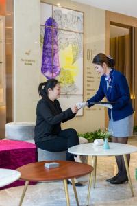 two women shaking hands in a room with tables at Lavande Hotels·Guangzhou Fangcun Jiaokou Metro Station in Guangzhou