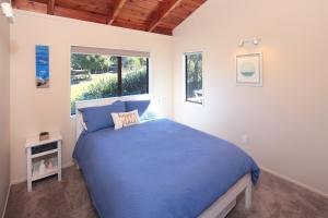 a bedroom with a blue bed and a window at Church Bay Views in Oneroa