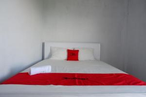 Una cama blanca con una almohada roja. en RedDoorz near Lokawisata Baturaden 2, en Tenjo