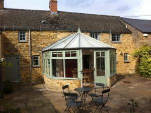 a conservatory with chairs and a table in front of a house at Keen Cottage in Kingham