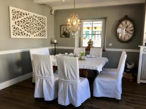 una sala da pranzo con tavolo, sedie bianche e orologio di Hotel zur Sonne a Rimsting