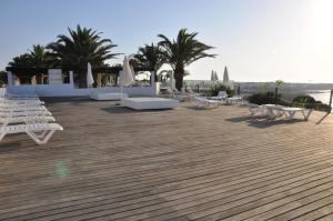 a patio with white chairs and tables and palm trees at Hotel Club Sunway Punta Prima in Es Pujols