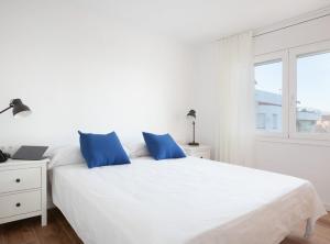 a white bed with blue pillows in a white bedroom at La Cala Beach Deluxe Apartments in L'Ametlla de Mar