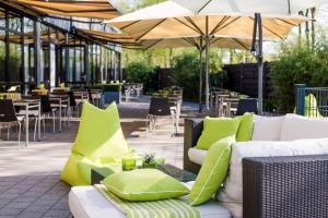 eine Terrasse mit Sofas, Stühlen, Tischen und Sonnenschirmen in der Unterkunft Novotel Nürnberg am Messezentrum in Nürnberg