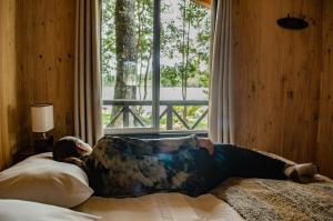 una persona sdraiata su un letto in una stanza con finestra di Cabañas Parque Michimahuida a Chaitén