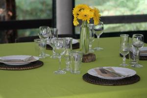 a green table with glasses and plates and a vase with a yellow flower at Woodlands Motel in Kerikeri