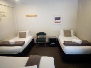 a small room with two beds and a chair at Woodlands Motel in Kerikeri