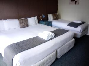 three beds in a hotel room with white sheets at Woodlands Motel in Kerikeri