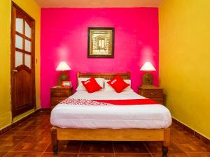 a bedroom with a pink wall and a bed with red pillows at OYO Posada De Los Angeles, Pátzcuaro in Pátzcuaro