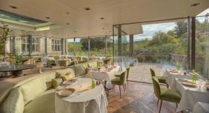 a restaurant with white tables and chairs and large windows at Gravetye Manor in East Grinstead