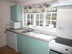 uma cozinha com armários azuis, um lavatório e janelas em Winterbourne Cottage em Chilmark