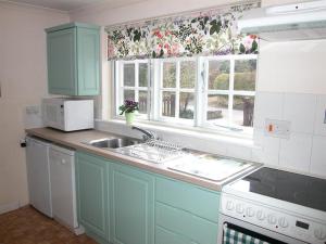 a kitchen with blue cabinets and a sink and windows at Winterbourne Cottage in Chilmark