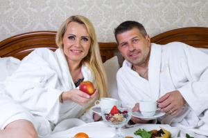 un homme et une femme assis au lit et mangeant de la nourriture dans l'établissement Bristol Kralovska Vila, à Karlovy Vary