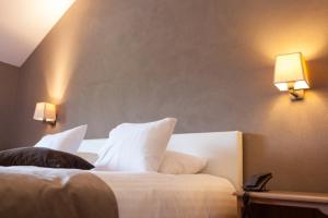 a bedroom with a bed with white pillows and two lights at Hotel La Passerelle in Grandhan