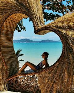 a woman sitting in a straw chair on the beach at Beach Houses in Rawai Beach