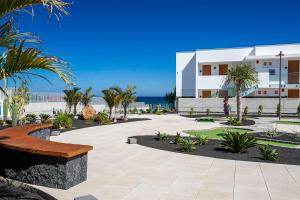 a building on the beach with palm trees and a bench at Hotel Lava Beach in Puerto del Carmen