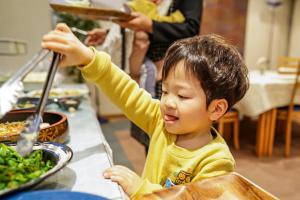 a young boy sitting at a table preparing food at Hotel Dorf Shizuoka in Shizuoka