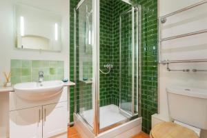 a green tiled bathroom with a shower and a sink at Veeve - South Kensington Garden Apartment in London