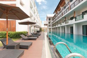 a swimming pool with chairs and umbrellas next to a building at Hotel MAYU Chiang Mai in Chiang Mai