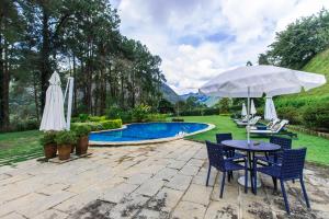 a patio with a table and chairs and an umbrella at Pousada Chácara Aracê in Araras Petropolis
