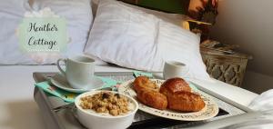 ein Tablett mit Croissants und Kaffee auf dem Bett in der Unterkunft Heather Cottage Aberdeen in Aberdeen