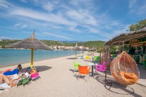 a group of people sitting on a beach with chairs and umbrellas at Apartments A-Z in Stara Novalja