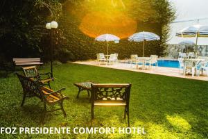 un grupo de sillas, mesas y sombrillas en un patio en Foz Presidente Comfort Hotel, en Foz do Iguaçu