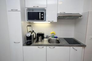 eine Küche mit weißen Schränken, einer Spüle und einer Mikrowelle in der Unterkunft Cozy Apartment close to Cornavin Train Station and lake in Genf