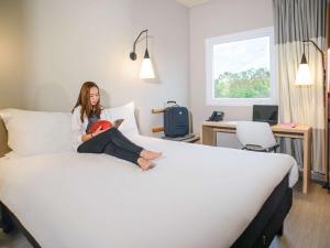 una mujer sentada en una cama en una habitación de hotel en ibis Itatiba, en Itatiba