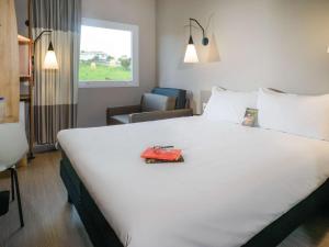 a hotel room with a large white bed and a chair at ibis Itatiba in Itatiba